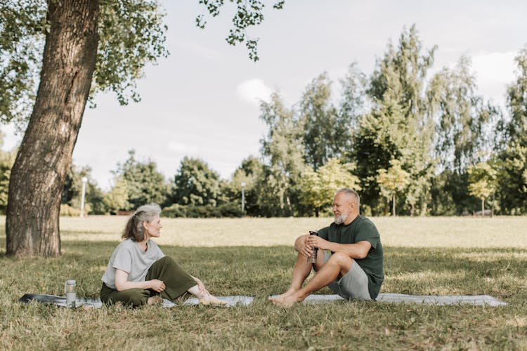 A Man And Woman Talking Together While Sitting On The Grass