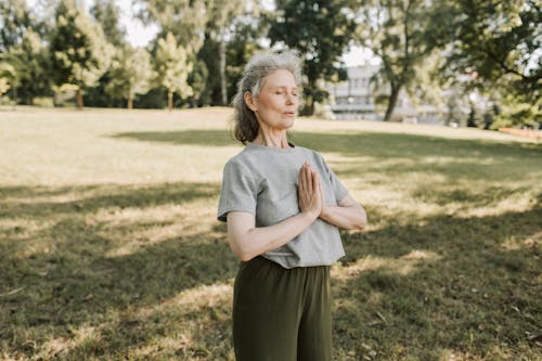 Elderly woman meditating and practicing yoga in a sunny park, embracing wellness and mindfulness.