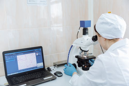 A Person in White Lab Gown Looking through Microscope