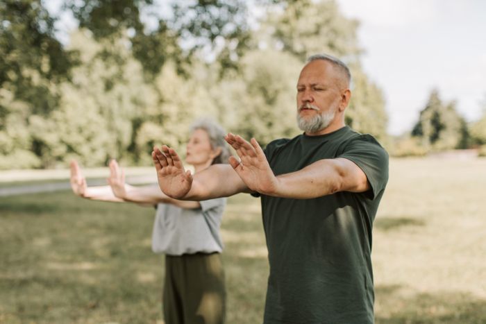 An older couple stretching arms wide during gentle outdoor yoga