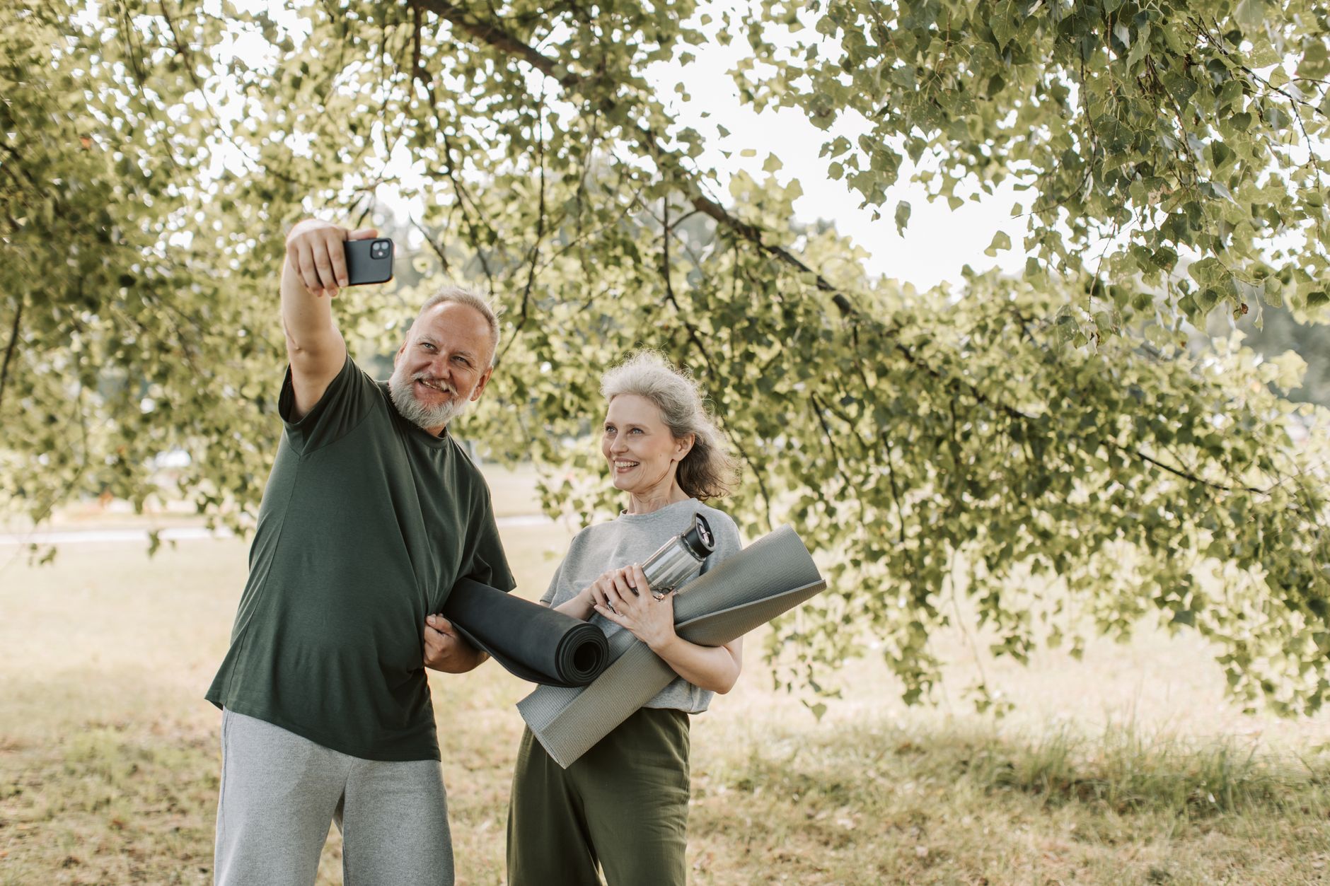 경남 어르신 스마트폰 무료 교육 4 A cheerful senior couple enjoys a sunny day outdoors, taking a selfie with their yoga mats.