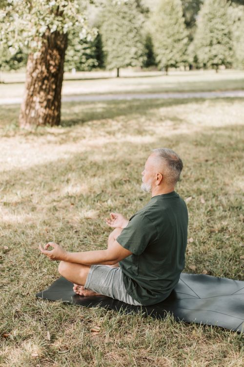 Free Senior man practicing yoga in a park, meditating in lotus pose on a sunny day. Stock Photo