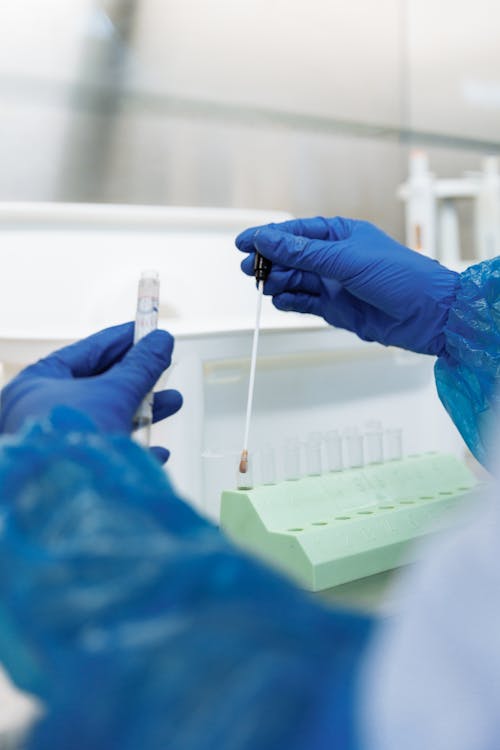 Free A Person Wearing Medical Gloves Holding a Test Tube and a Medical Swab Stock Photo