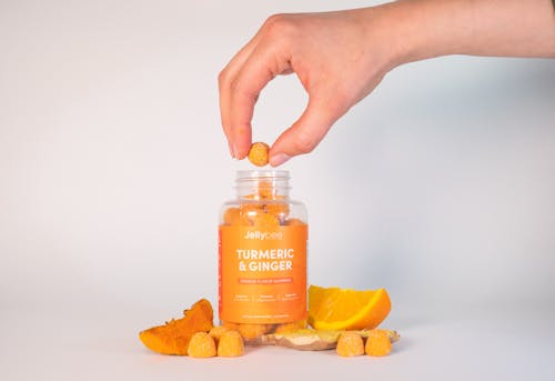 Free Person Holding A Gummy From an Orange Plastic Bottle Stock Photo