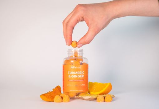 Person Holding A Gummy From an Orange Plastic Bottle