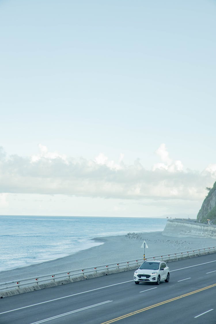 A White Car Passing A Road By The Beach