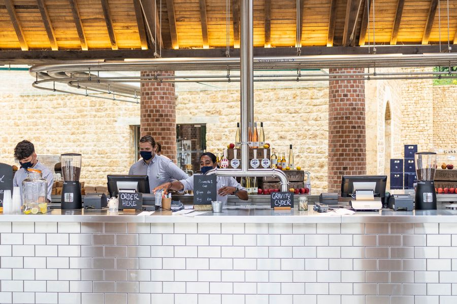 Employees at a modern cafe counter serving customers while wearing masks, indoors.