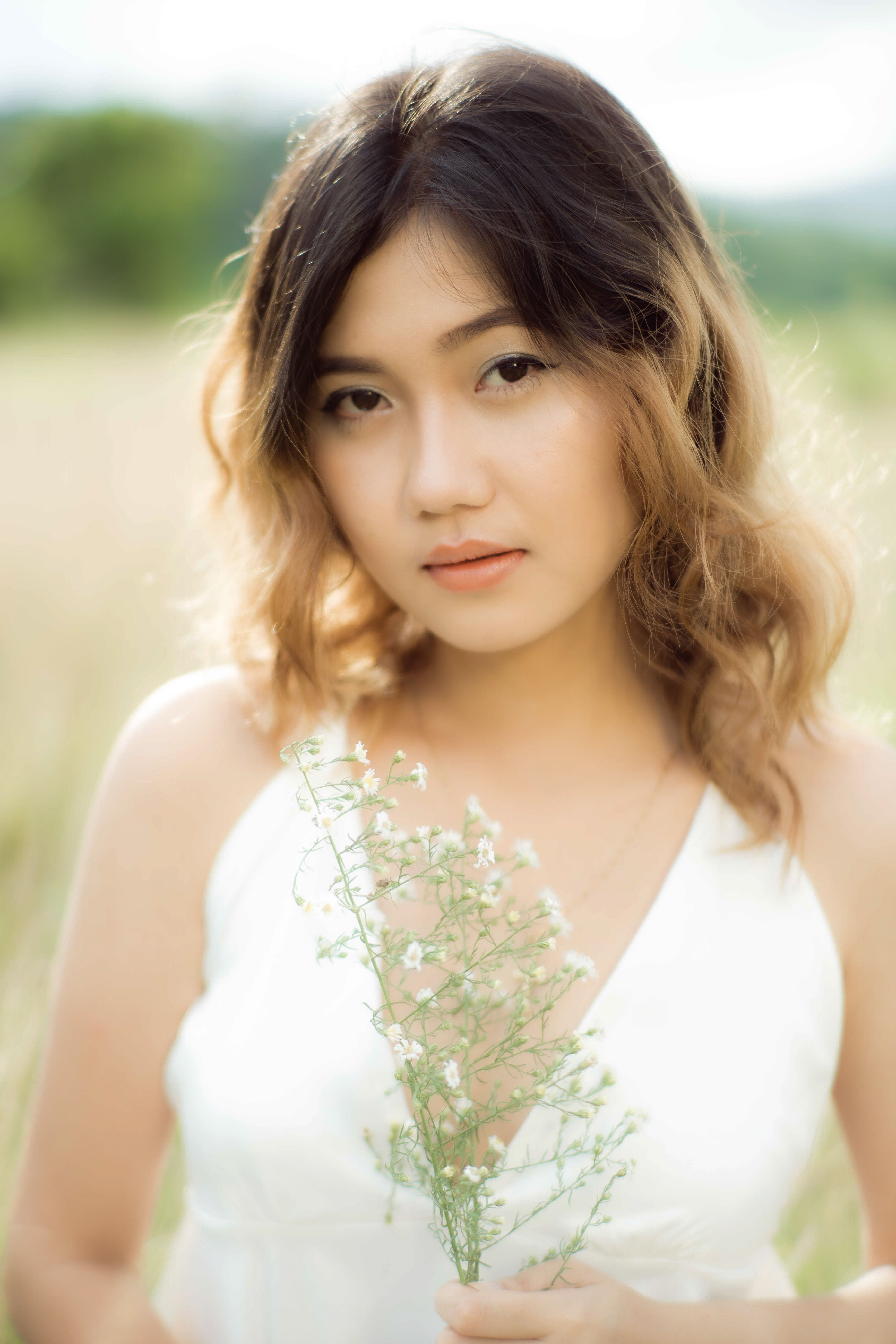 A stunning portrait of a young woman holding delicate white flowers in a sunny outdoor setting.