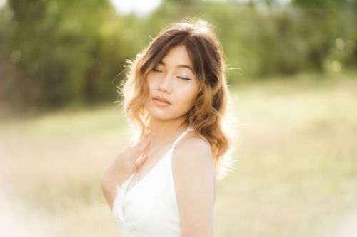 Free An Asian woman in a white dress poses gracefully with eyes closed in a sunny field. Stock Photo
