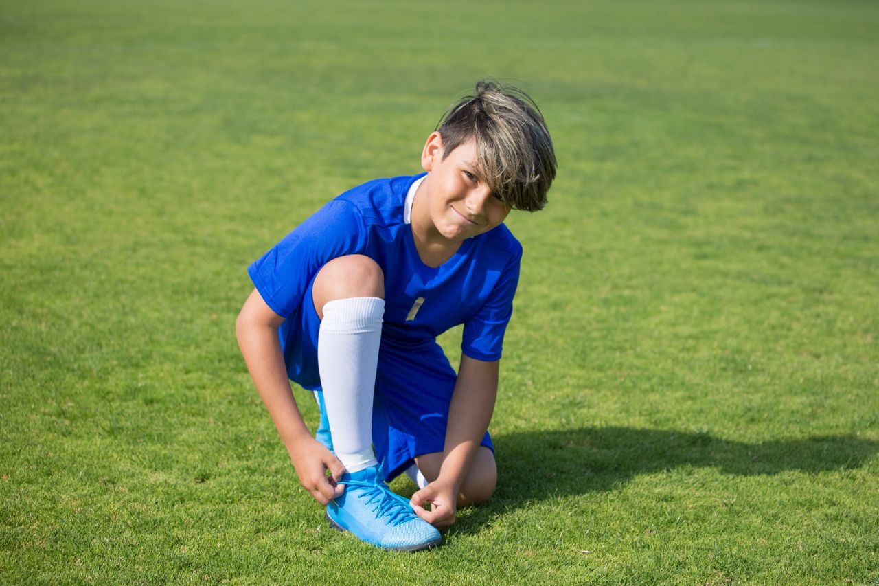 a young soccer player ties his shoelaces on a sunny day outdoors prepa