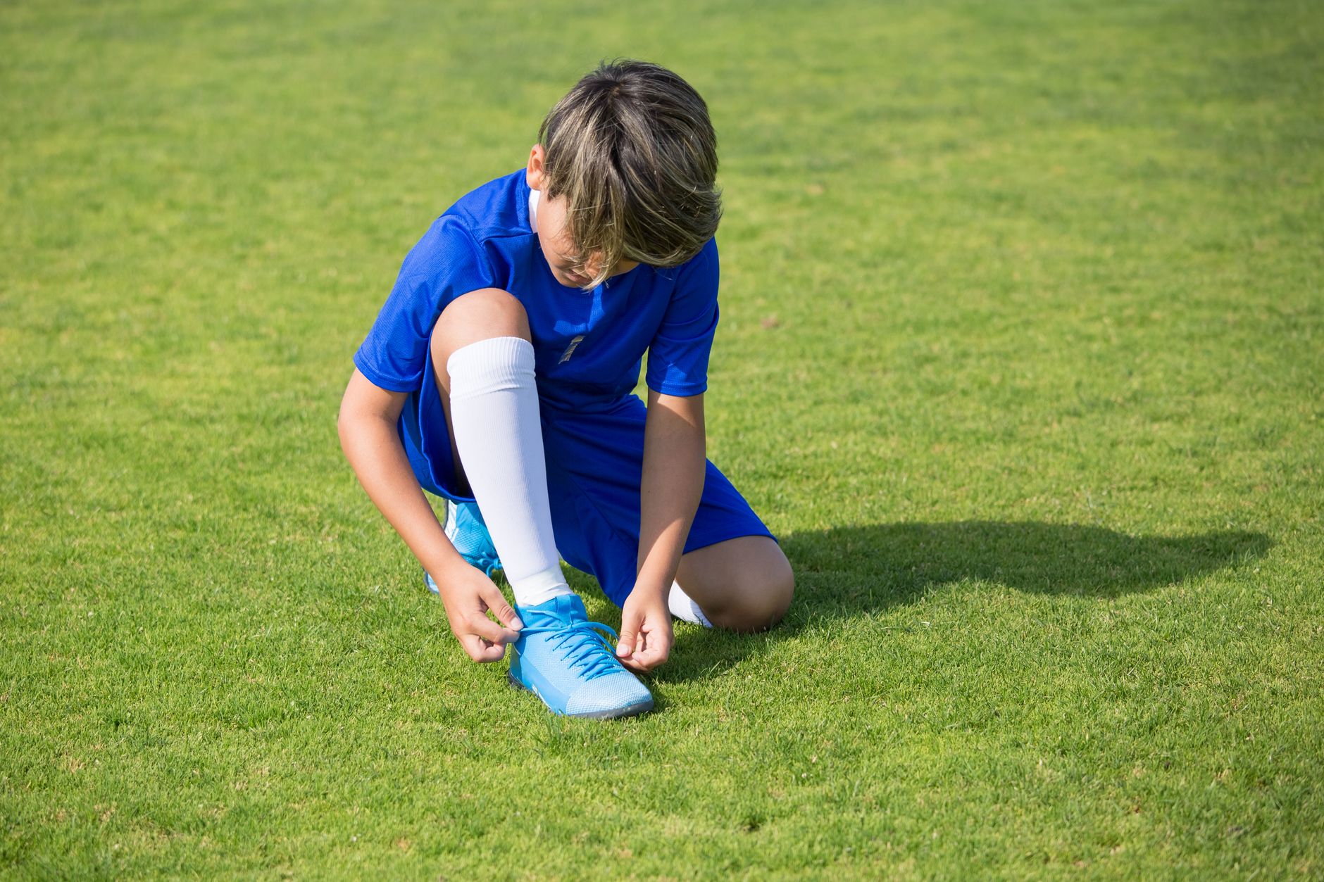beginner football player tying Nike Premier cleats beside a marked grass training pitch