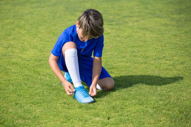 Boy In Blue Soccer Uniform Tying His Shoe