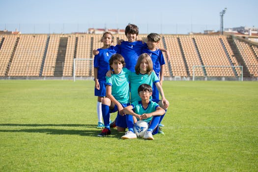 Group of young boys in soccer uniforms posing with a ball on a football field.