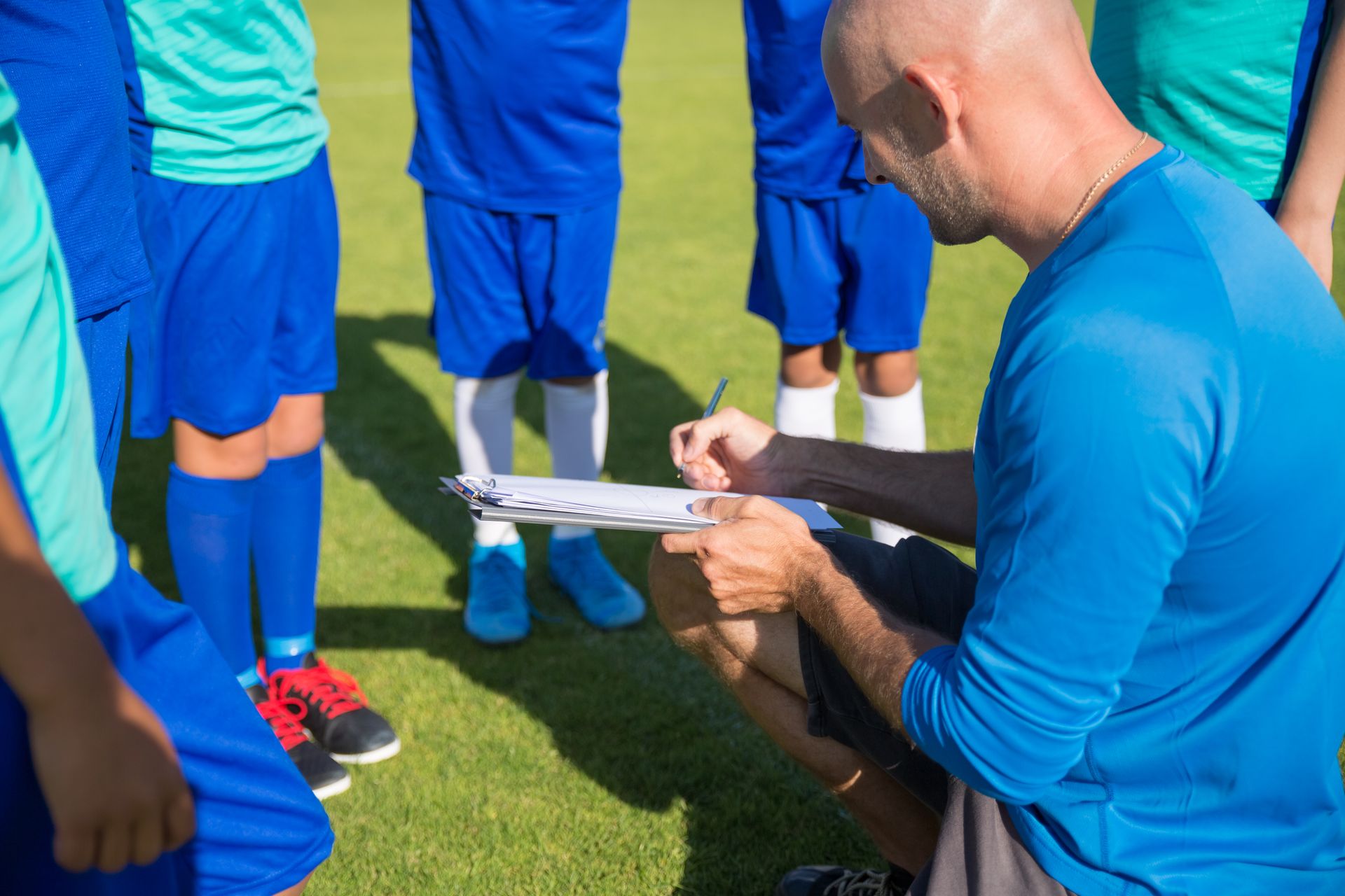 A youth soccer coach reviewing strategy on a clipboard with his team