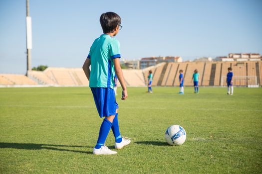 Young kids playing soccer on a sunny day in an open field, wearing uniforms.