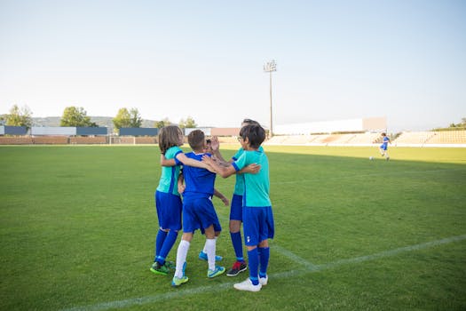 A group of young soccer players in blue uniforms celebrating together on a sunny field.