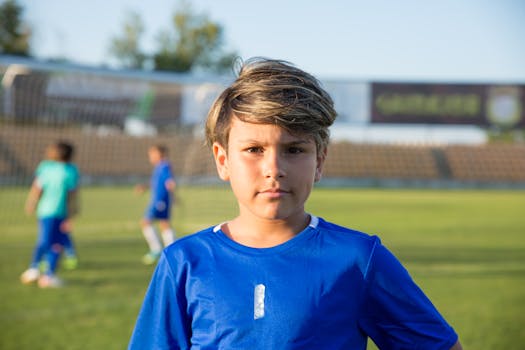 A young boy stands on a soccer field in Portugal, ready for practice under clear skies.