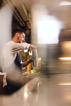 Side view of a bartender skillfully mixing a drink with a shaker indoors.