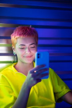 A stylish young woman with short hair using smartphone in vibrant neon lighting.