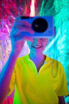 A young woman joyfully captures a selfie amidst vibrant, colorful neon lights.