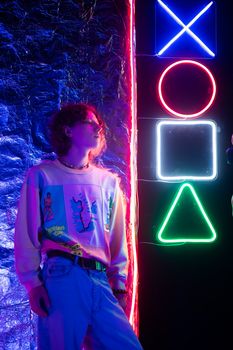 A young adult stands in a neon-lit setting with colorful symbols and retro style.