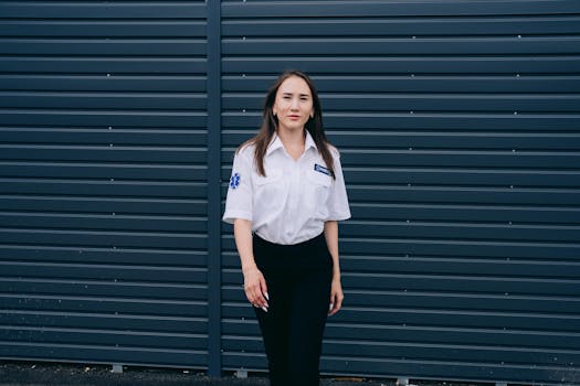 A female paramedic standing confidently against a dark metal wall, showcasing professional attire.