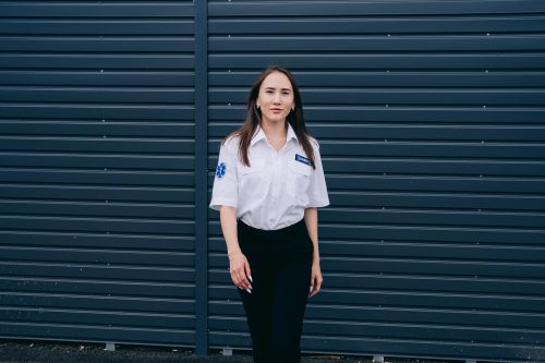 Free A female paramedic standing confidently against a dark metal wall, showcasing professional attire. Stock Photo