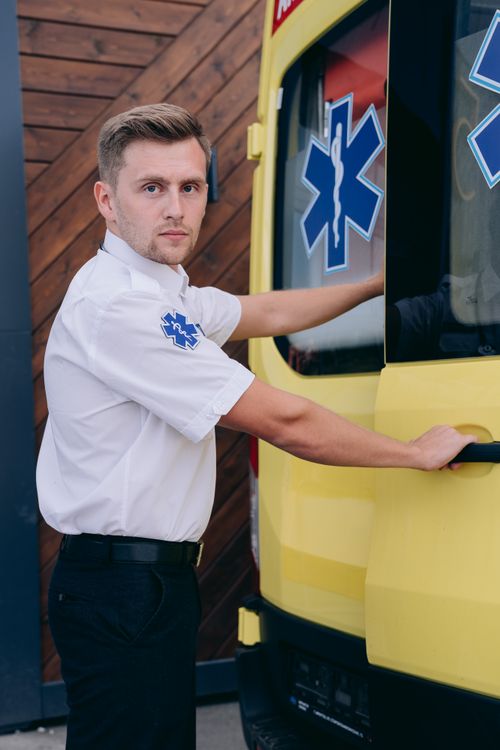 Free Paramedic in uniform standing by and holding ambulance door handle outside. Stock Photo