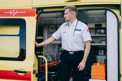 Free Paramedic standing by an ambulance, ready to assist in emergencies with medical equipment. Stock Photo