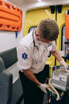A paramedic wearing a mask operates medical equipment inside an ambulance.