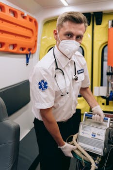 A paramedic in a mask prepares medical equipment inside an ambulance, focusing on emergency healthcare.
