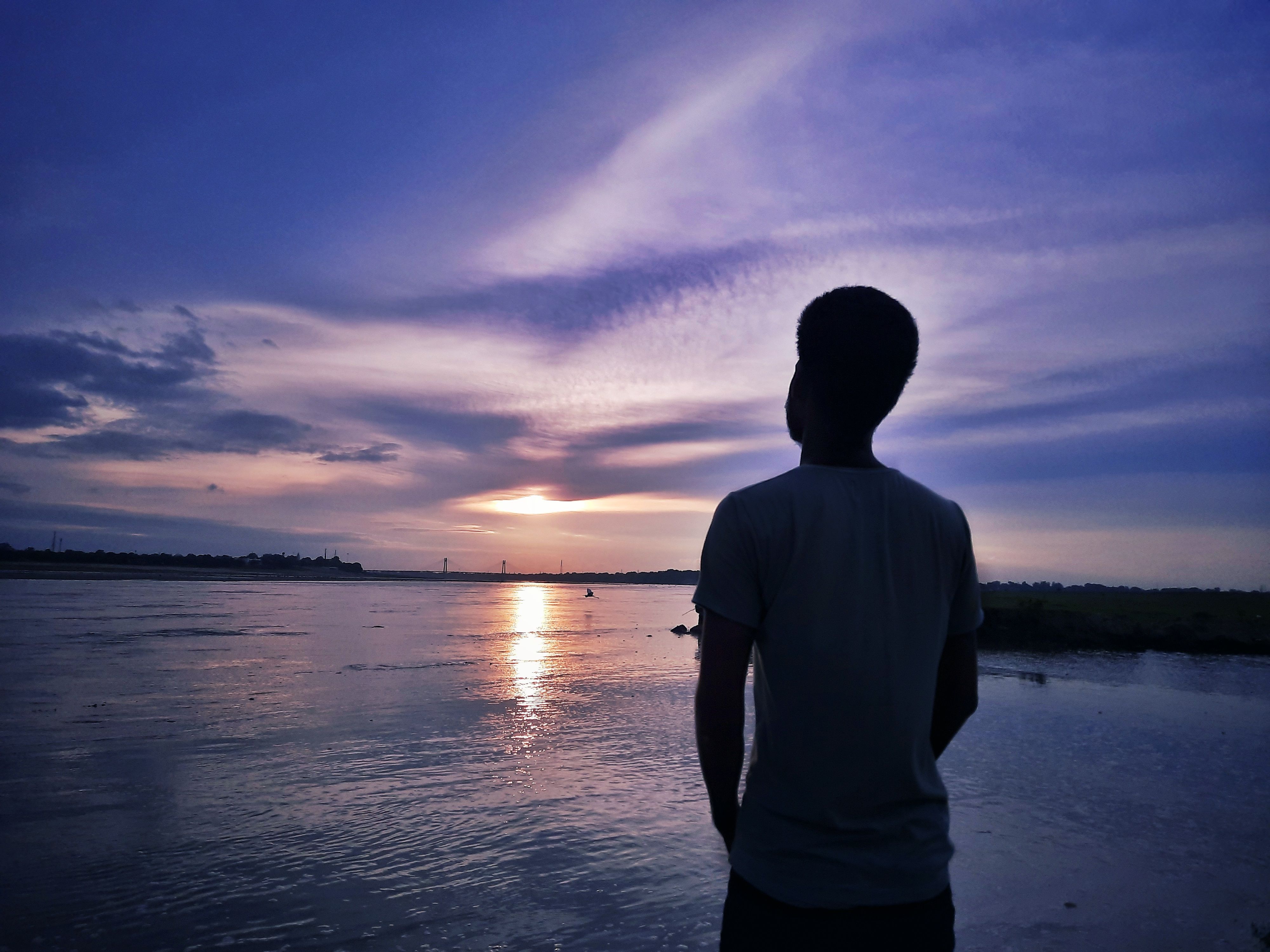 A solitary figure stands by the waterside watching a calm and beautiful sunset.