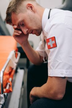 A paramedic in uniform appears stressed sitting beside a stretcher in an ambulance.