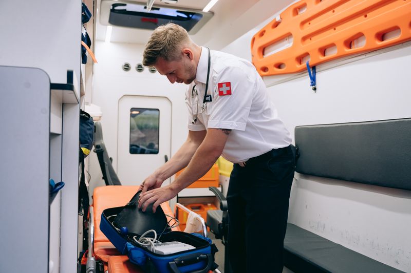 A paramedic organizing medical equipment in an ambulance interior.