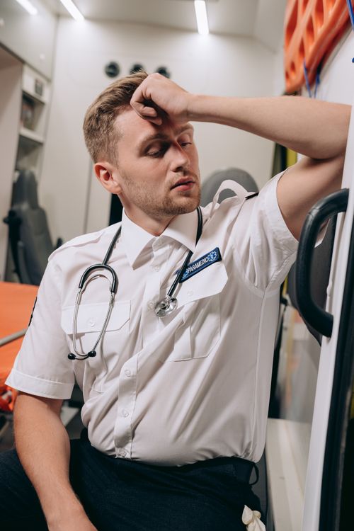 Free A paramedic sits inside an ambulance, hand on forehead, appearing exhausted. Stock Photo