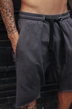 Detailed view of a man's tattoo and fashion shorts with hand in pocket.