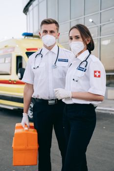 Paramedics in protective masks stand ready by their ambulance, showcasing healthcare dedication.