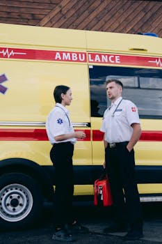 Male and female paramedics standing next to a yellow ambulance, preparing for emergency response.