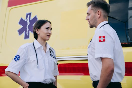 Two paramedics in uniform stand by an ambulance, ready for action.