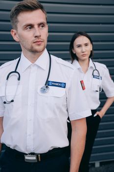 Two paramedics in white uniforms standing attentively outdoors, ready for action.
