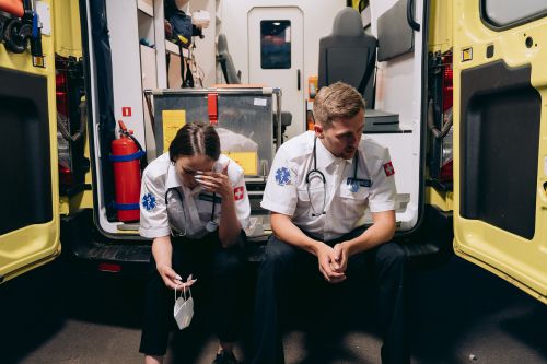 Free Two paramedics sitting tired at the back of an ambulance, reflecting the stress of emergency services. Stock Photo