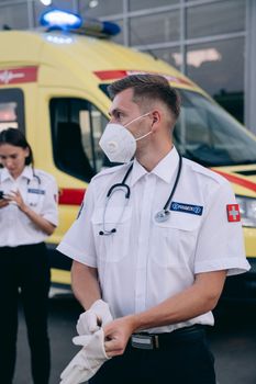 Two paramedics in protective gear getting ready near an ambulance.