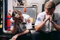 A Pair of Paramedics Sitting on Ambulance Bumper with Regretful Reactions