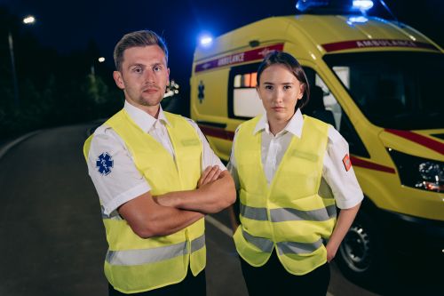 Free Two medical professionals in reflective vests stand confidently by an ambulance at night. Stock Photo