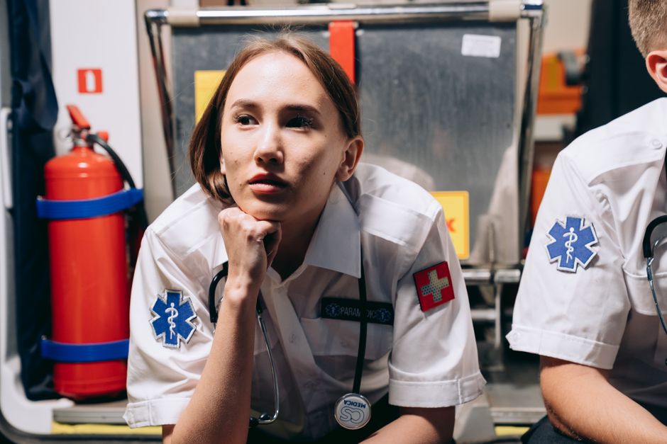 Fotomural Una paramédica femenina descansa con una expresión pensativa mientras está sentada junto a equipos de emergencia.