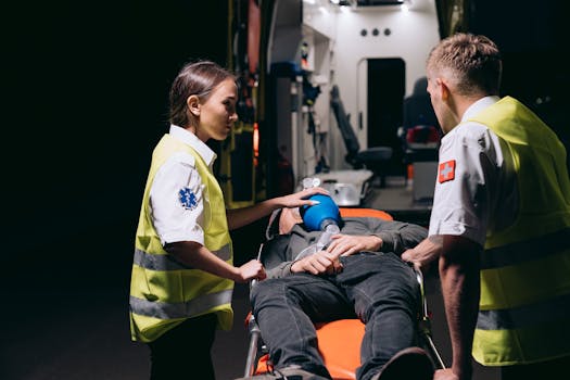 Paramedics in reflective uniforms assist a patient on a stretcher near an ambulance at night.