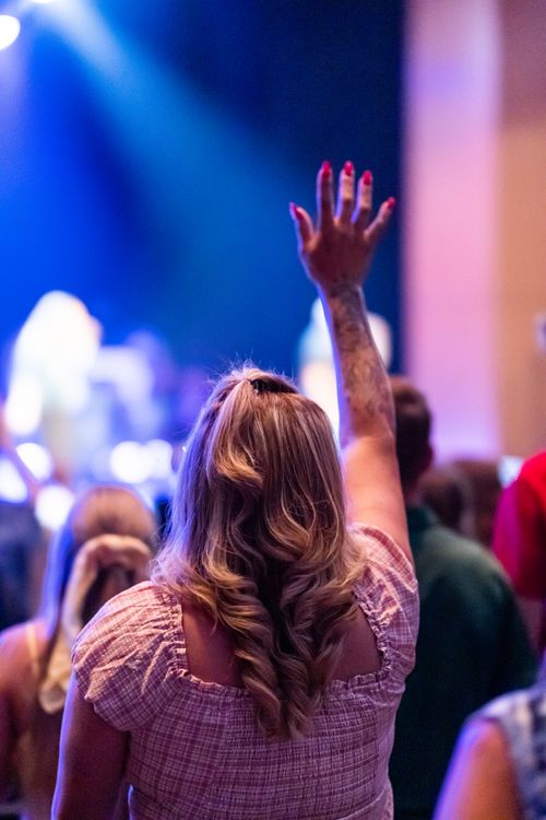 Free A woman raises her hand in worship during a vibrant indoor music concert. Stock Photo