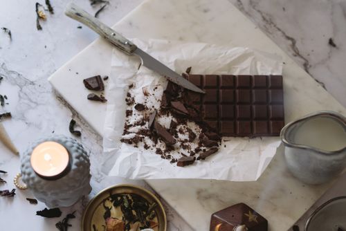 Free Aesthetic arrangement of chocolate bar with knife on marble near candle and pottery jug. Stock Photo