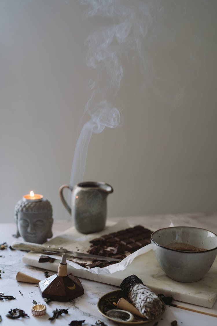 A Lighted Incense Near A Bar Of Chopped Chocolate On A Chopping Board