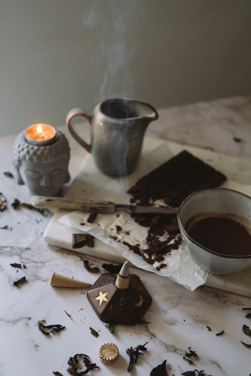 Free Burning Candle and Incense Standing on a Table next to a Chocolate Bar and Ceramic Dishes  Stock Photo